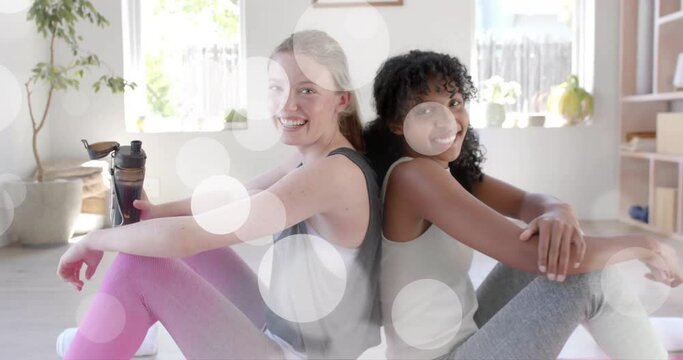 Animation of light spots over happy diverse teenage girls relaxing after practicing yoga