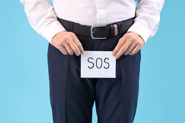 Young businessman holding paper with word SOS on blue background, closeup. Prostate cancer...