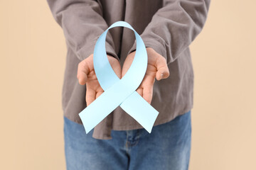 Young man with blue ribbon on beige background, closeup. Prostate cancer awareness concept