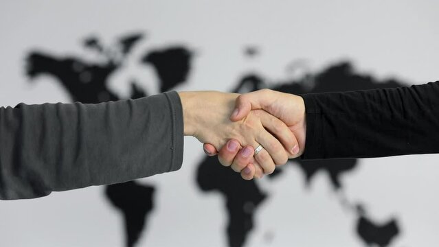Handshake of two men near black world map on white wall