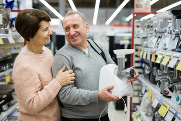 Happy European spouses of mature age, who have come to an electronics and home appliance store choose an electric meat grinder ..to buy it