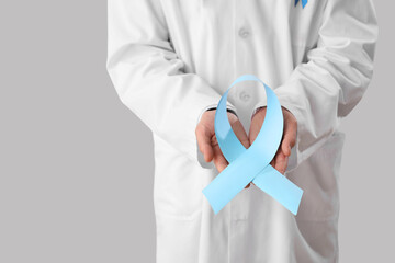 Male urologist with blue ribbon on light background, closeup. Prostate cancer awareness concept
