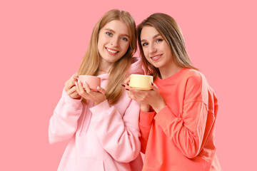 Beautiful young women with cups of tea on pink background