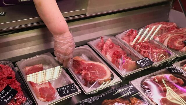 Hand takes tray with gammon from showcase with other kinds of meat in store