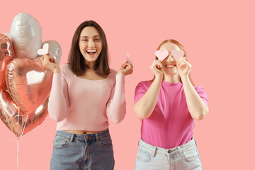 Young lesbian couple with paper hearts and balloons on pink background. Valentine's Day celebration