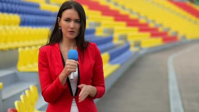 Reporter with microphone speaks near seats on sports stadium