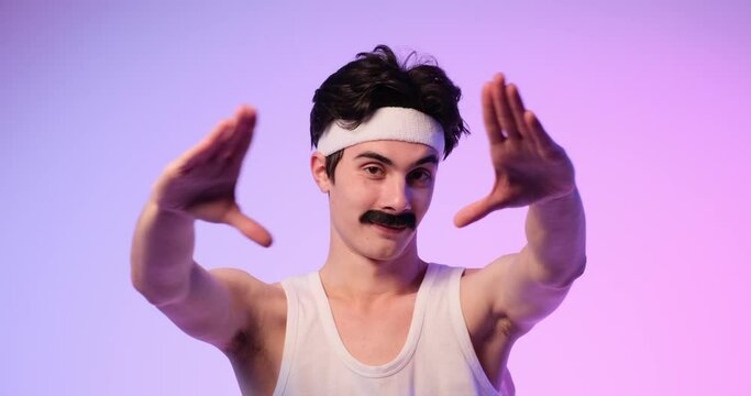 Caucasian freaky 80-90s young man in love showing heart shape by hand in symbol of valentine day, love, affection, standing over purple background.