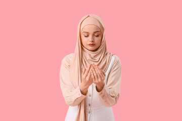 Young Muslim woman in hijab praying on pink background