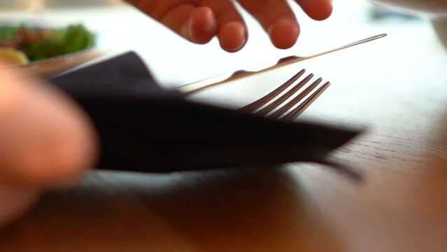 Close-up of cutlery, fork and knife wrapped in a black napkin on a table in a fancy restaurant. A woman's hand takes a knife.