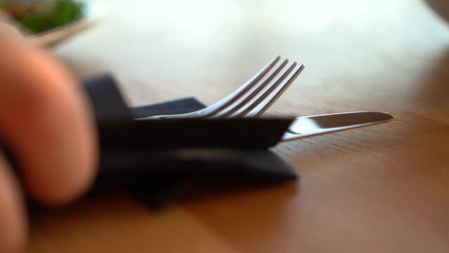 Close-up of cutlery, fork and knife wrapped in a black napkin on a table in a fancy restaurant. the entire kit with a napkin and escapes from the frame