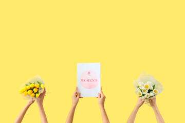Female hands with bouquets of tulips and festive postcard on yellow background. International Women's Day celebration