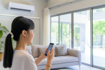 Modern living concept with an Asian woman adjusting air conditioning using a smartphone app indoors.

