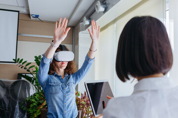 woman with curly hair wearing VR in the office collaborating with asian colleague in front of her