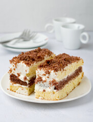 Two pieces of cake on a plate, coffee cups, milk jug, cutlery on a light background.