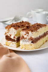 Two pieces of cake on a plate, coffee cups, milk jug, cutlery on a light background.