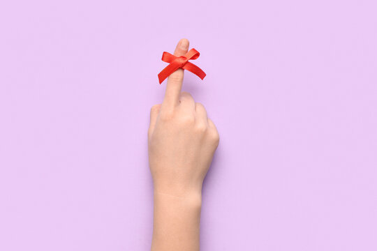 Female hand with red bow on index finger against lilac background. Reminder concept
