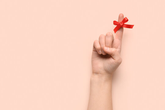 Female hand with red bow on index finger against pink background. Reminder concept