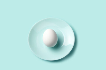 Table setting single white egg centered on a pastel blue plate, embodying minimalistic design and Easter simplicity. Greeting card for spring and Easter projects.