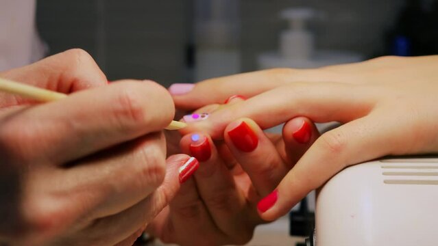 Woman adorns girls nails by colorful circles in beauty salon