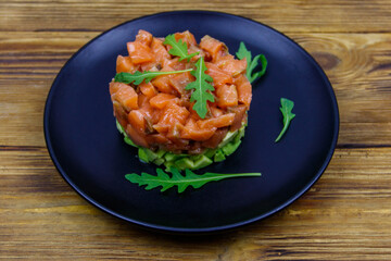 Salmon tartare with avocado and arugula on wooden table