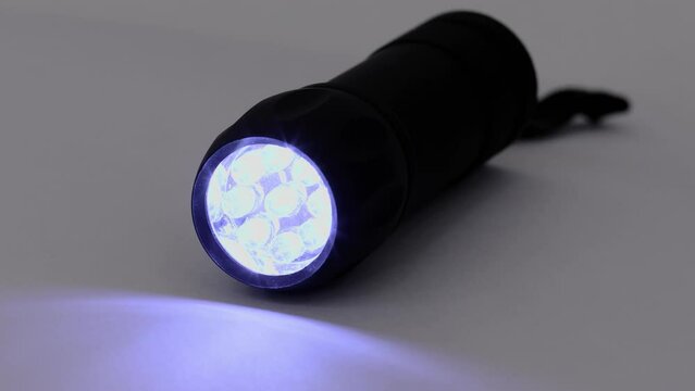Black led flashlight runs and rotates on white surface