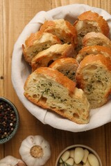 Tasty baguette with garlic and other spices on wooden table, flat lay