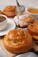 Pouring honey onto delicious rolls with raisins at table, closeup. Sweet buns