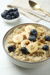 Tasty oatmeal with banana, blueberries, walnuts and honey served in bowl on white wooden table, closeup
