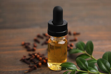 Clove oil in bottle, leaves and dried buds on wooden table, closeup