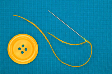 yellow button, needle and thread on blue fabric