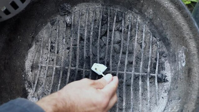 Man kindles piece of paper on barbecue grid. Slow motion