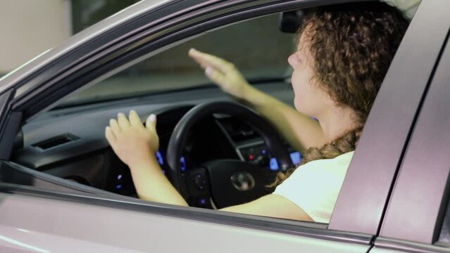 Woman sits on drivers place in car and drums at dashboard