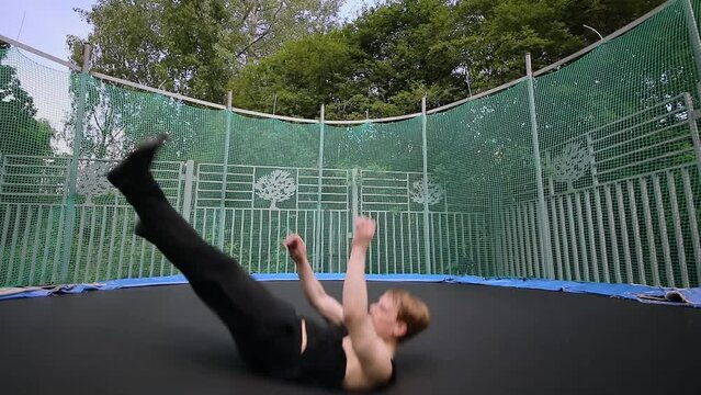 Yong man jumps on outdoor trampoline and makes somersaults. Slow motion