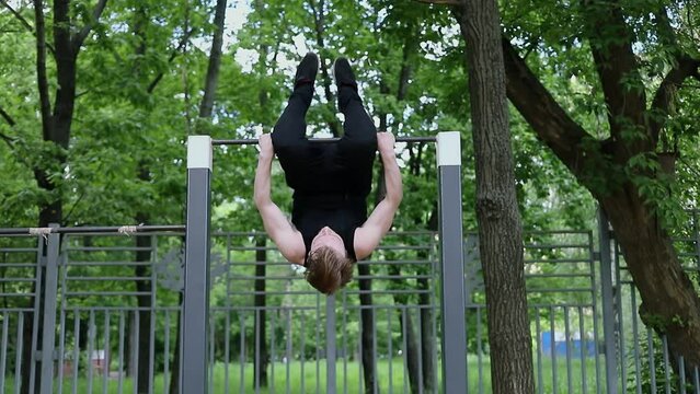 Young man does exercise on bar among trees. Slow motion