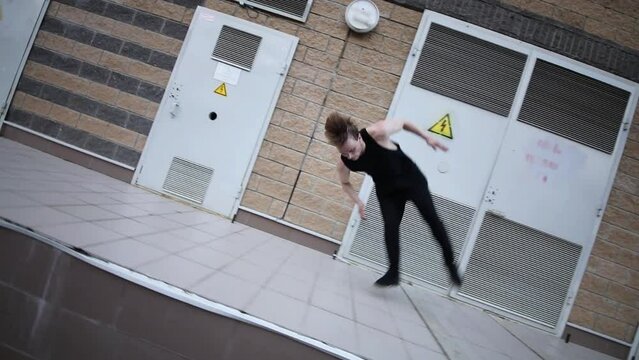 Young man runs and makes somersault near doors of electric premises. Slow motion