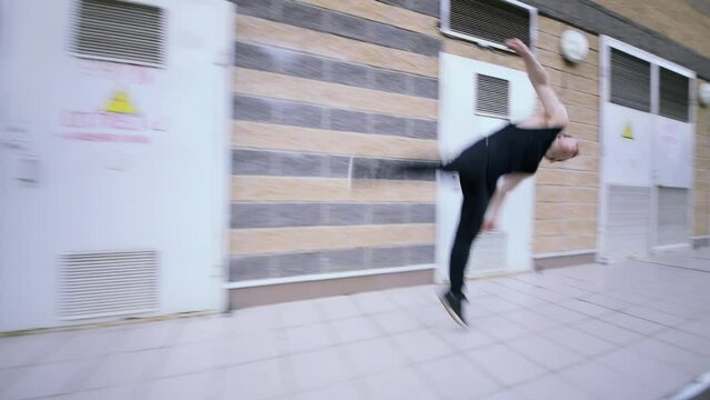 Young man runs and does side-flip near doors of electric premises. Slow motion