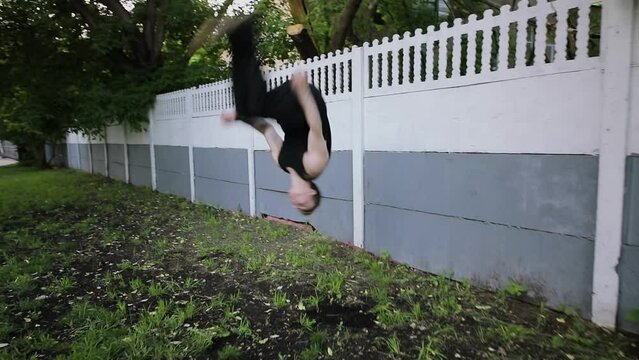 Young man pushes off from wall, makes back-flip and runs away. Slow motion