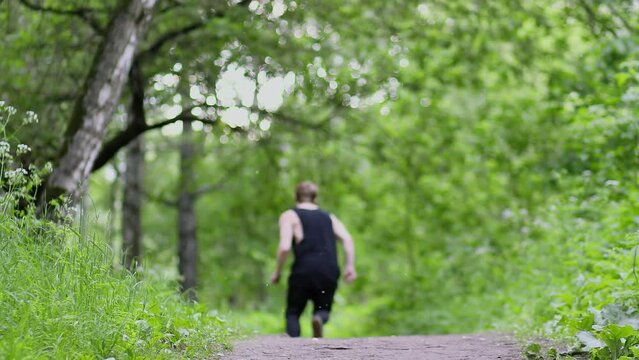 Young man runs and does somersault during parkour training on footpath in park. Slow motion