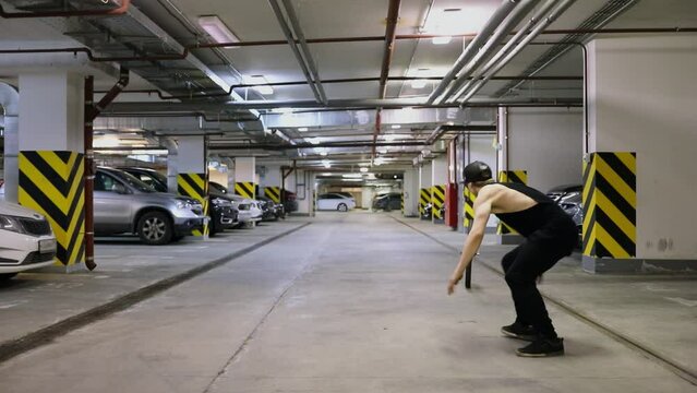 Young man jumps with salto over rolling wheel in underground garage. Slow motion