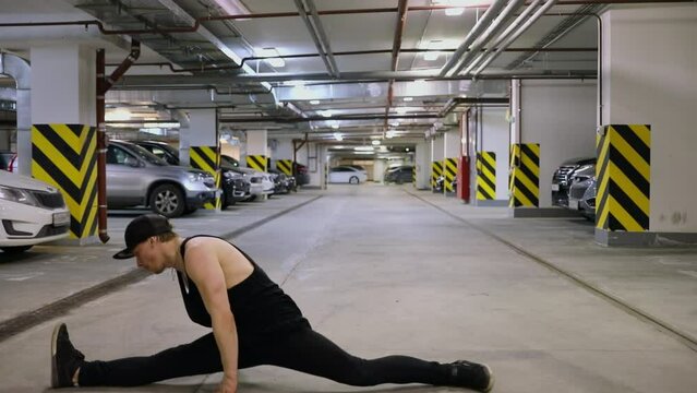 Young man does somersault and splits on floor at underground parking. Slow motion