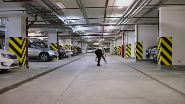 Young man runs and makes somersault at underground parking. Slow motion