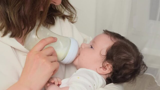 Mother gently nourishes her baby girl, using a petite baby bottle, and gazes at her daughter
