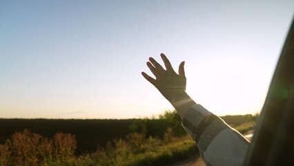 Road trip female hand from window of driving car at sunset sunrise rural summer field closeup. Woman arm enjoy freedom air travel adventure active lifestyle automobile journey exploration discovery - obrazy, fototapety, plakaty