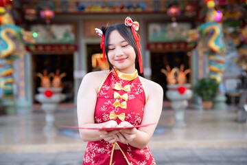 Portrait smiles Asian young woman wearing red cheongsam dress holding red envelopes decoration for Chinese new year festival celebrate culture of china at Chinese shrine Public places in Thailand