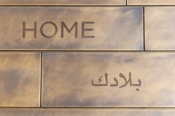 The word home in English and Arabic on a tile wall.