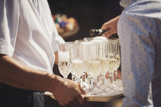 Waiter carries glasses with cold champagne. Waiter pours champagne in glasses. Catering service, banquet. green on the left side of the photo. official event.