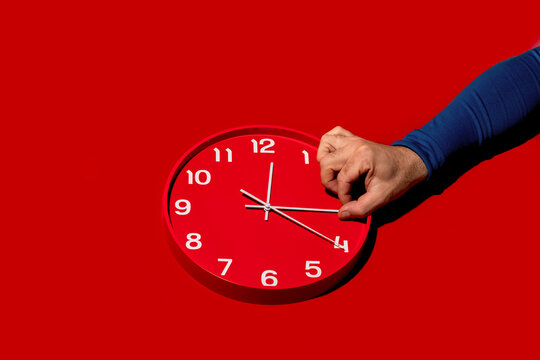 Adjusting time on red wall clock against bold background
