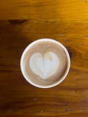 Closeup of a vegan latte with heart foam art made with oat milk, on a wooden table with soft natural light.