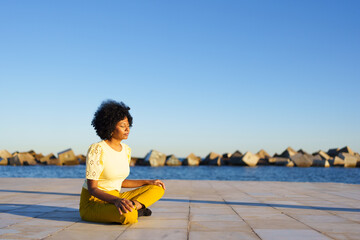 Horizontal photo with copy space of an african woman meditating sitting next to the sea