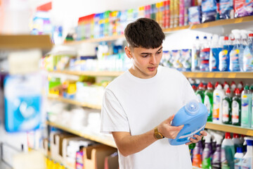 in supermarket, man carefully chooses detergent for dishes